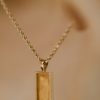 gold rectangular pendant necklace on white surface